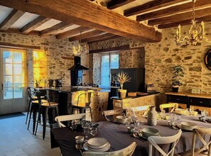 A rustic kitchen with stone walls, wooden beams, a chandelier, and a dining area set for a meal. - La Pierre du Bonheur" village house for 2 to 8 people (Saint-Denis-d'Anjou)