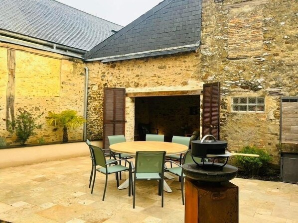 A stone building with a round table and chairs, a fireplace, and a small window.