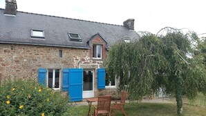 A stone house with a grey roof, a small window, and a door with blue shutters. There is a wooden table and two chairs in the front yard. - Typical Breton house between the Gulf of Morbihan and the ocean (Pluneret)