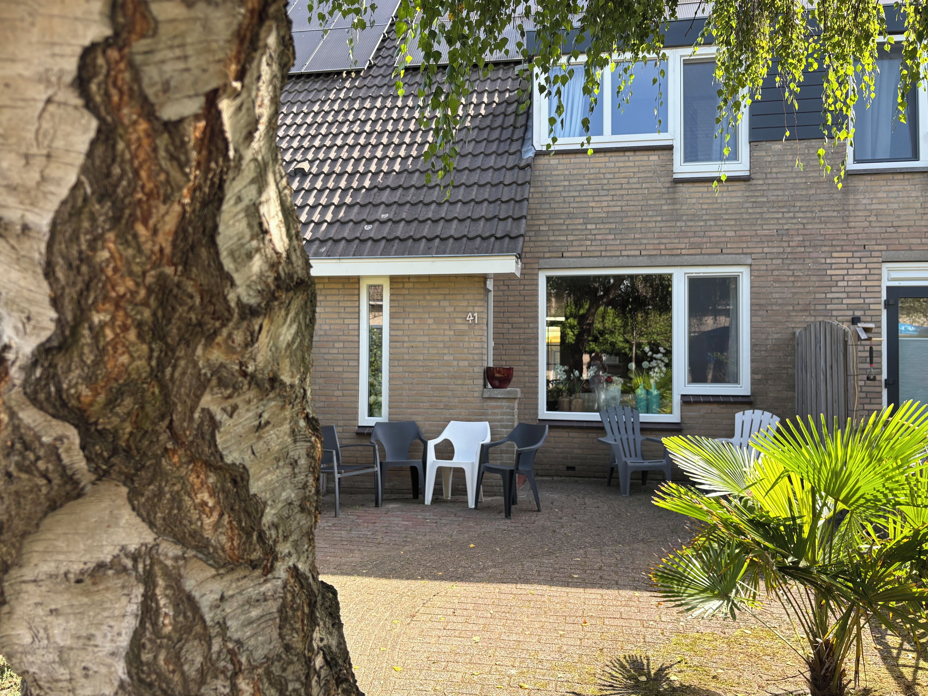 A residential building with a tiled roof, brick walls, and a brick patio with outdoor furniture.
