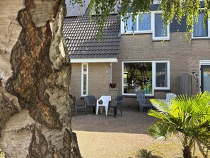 A residential building with a tiled roof, brick walls, and a brick patio with outdoor furniture.