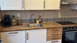 Een kleine keuken met witte kasten, een roestvrijstalen spoelbak en een zwarte oven.