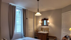 A bedroom with a bed, bedside table, lamp, window with curtains, wooden dresser, vanity with mirror, and a chair. - Comfortabele en charmante kamer Montravel in de nummer 1 B&B van Ribérac. (Ribérac)