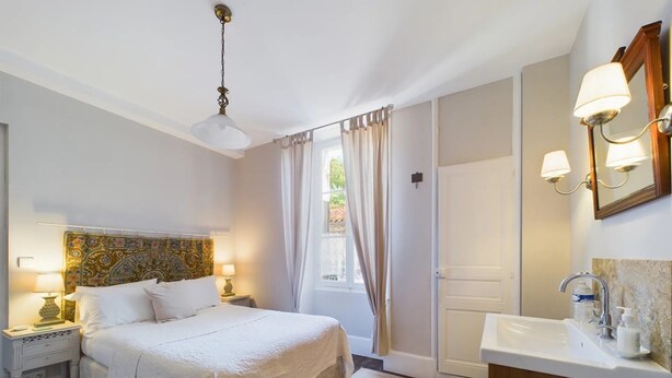 A hotel room with a bed, nightstands, a mirror, a sink, and a window with curtains. - Comfortabele en charmante kamer Montravel in de nummer 1 B&B van Ribérac. (Ribérac)