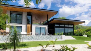 A modern two-story house with a flat roof, large windows, and a stone wall. - Casa Armonía - New Luxury Ocean View Villa - Walking distance to the beach! (Playa Hermosa)