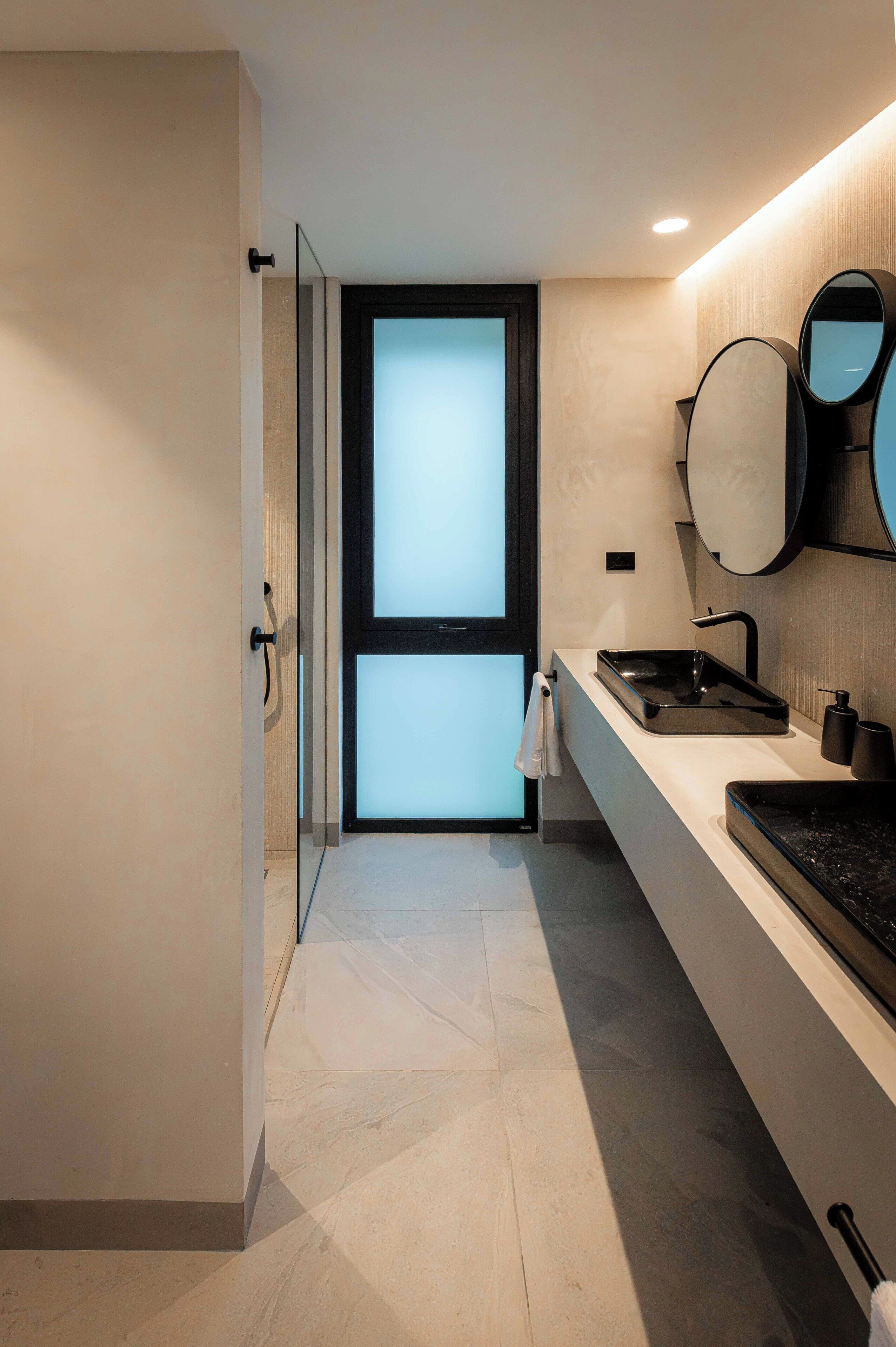 A modern bathroom with a glass door, a black sink, and a mirror.
