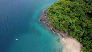 An aerial view of a beach with clear turquoise waters, a rocky shoreline, and dense green vegetation. - Casa Armonía - New Luxury Ocean View Villa - Walking distance to the beach! (Playa Hermosa)