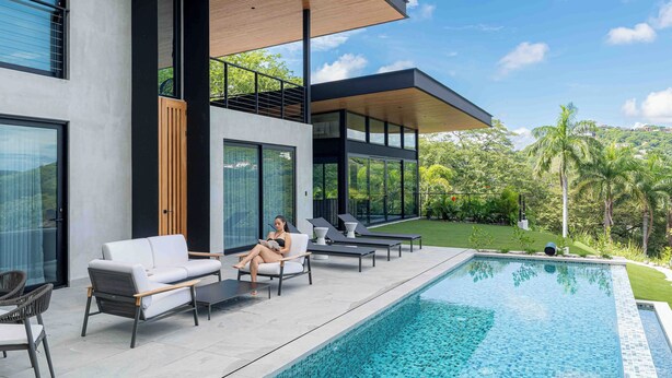 A modern outdoor pool area with a minimalist design, featuring a pool, lounge chairs, and a glass-enclosed patio. - Casa Armonía - New Luxury Ocean View Villa - Walking distance to the beach! (Playa Hermosa)