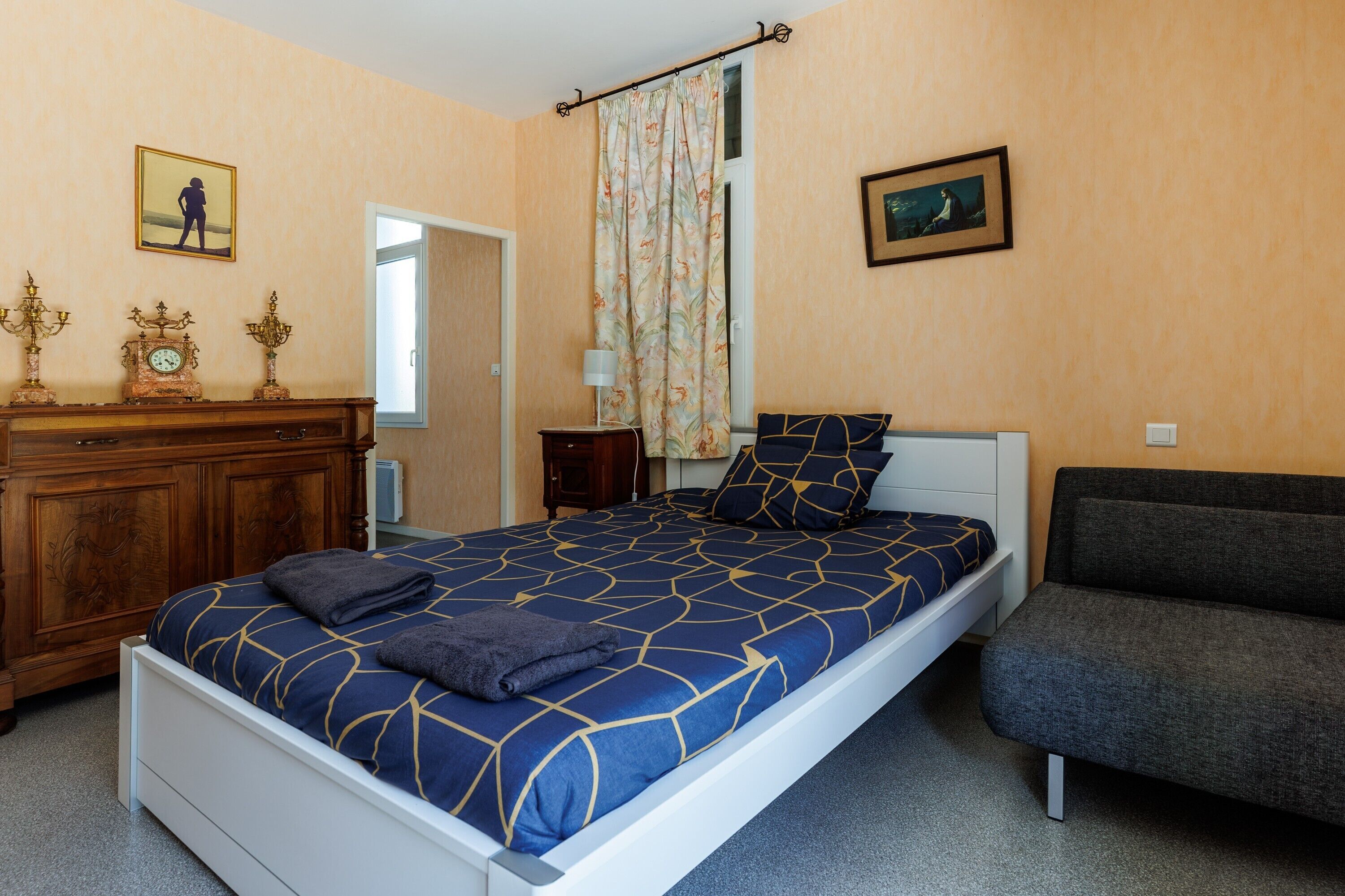 A bedroom with a bed, a dresser, a nightstand, a chair, and two framed pictures on the wall.