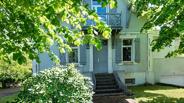 Una casa de dos pisos con una puerta principal, una escalera que conduce a la entrada y un pequeño jardín.