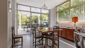 Un comedor con mesa y sillas de madera, ventanas amplias con vista a la vegetación y una lámpara de techo.