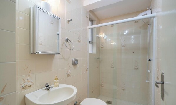 Un baño con ducha, inodoro, lavamanos y espejo.