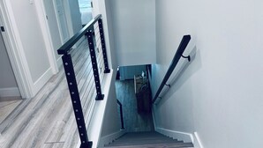 Una scala con ringhiera in metallo nero, gradini in legno e parete bianca.