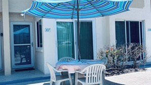 Una terrazza con tavolo e sedie, un ombrellone e un edificio con numeri sulle porte.
