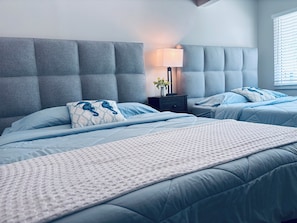 A bedroom with a tufted headboard, two beds with matching bedding, a bedside table with a lamp, and a window with blinds. - Siesta Key Beach Townhouse - Walk to Beach - 2BR - Pool & Parking (Siesta Key)