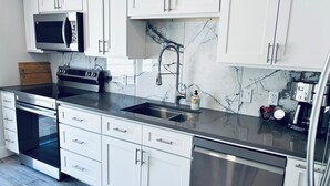 Una cucina moderna con mobili bianchi, elettrodomestici in acciaio inossidabile, una schiena di marmo e un forno a microonde integrato.