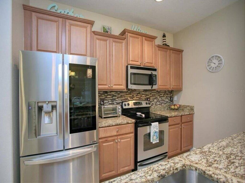 A kitchen with wooden cabinets, stainless steel appliances, granite countertops, and a clock on the wall.
