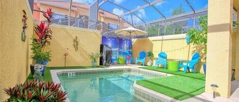 A pool area with a glass ceiling, artificial grass, and blue chairs.