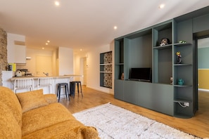 A modern living room with a sofa, a TV, and a kitchen area in the background. - 'New Duplex in City Center' Apartment – Ideal for Spa Guests with Balcony – Conciergerieland (Dax)