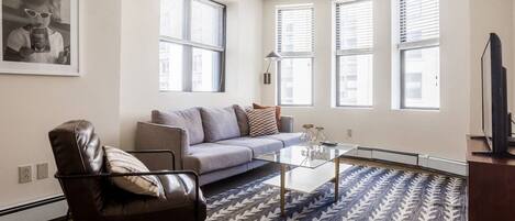 A modern living room with a leather chair, a grey sofa, and a patterned rug.