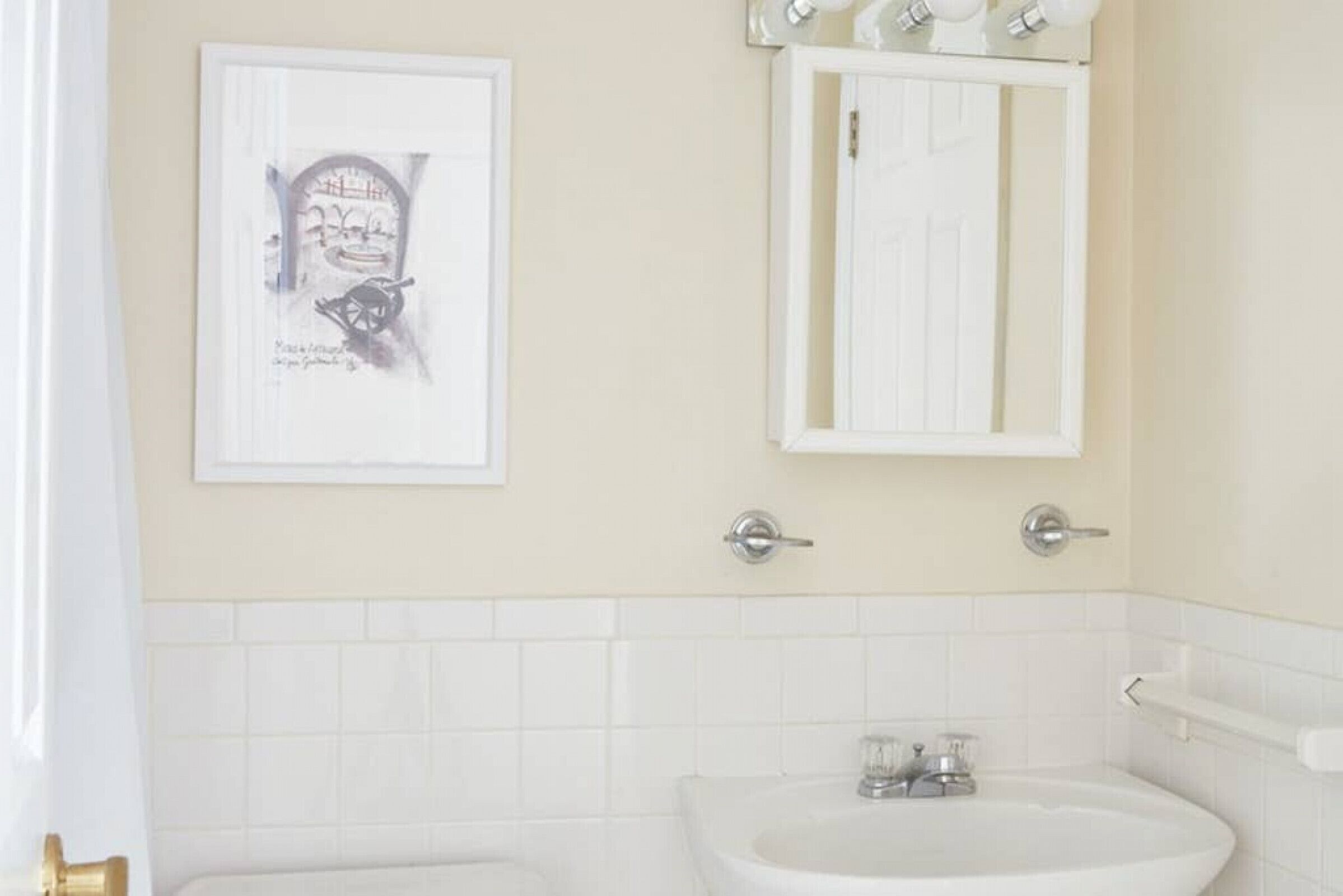 Un baño con un lavamanos blanco, un espejo y un cuadro enmarcado en la pared.