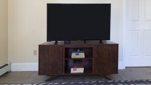 A dark wooden TV stand with a flat-screen TV on top, two shelves with books, and a patterned rug on the floor. - New to VRBO!  Awesome location downtown, closeby bars, restaurants + historic sites Walk Anywhere! (Boston)