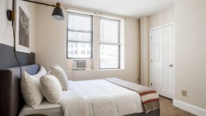 A bedroom with a bed, a bedside table, a lamp, a window with blinds, and a door. - New to VRBO!  Awesome location downtown, closeby bars, restaurants + historic sites Walk Anywhere! (Boston)