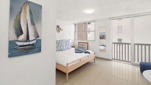 Une chambre à coucher avec un lit, un tableau représentant un voilier, une fenêtre et un balcon.
