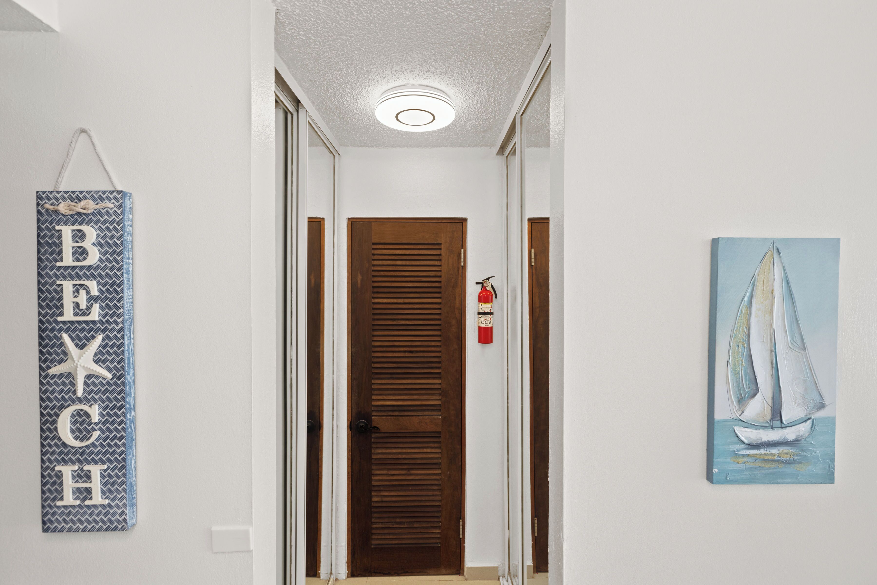 Un pasillo con una puerta de madera, un extintor y un cuadro de un velero.