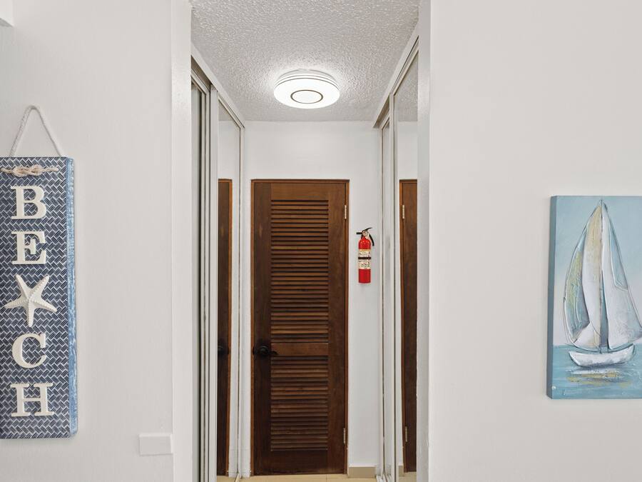 Un pasillo con una puerta de madera, un extintor y un cuadro de un velero.