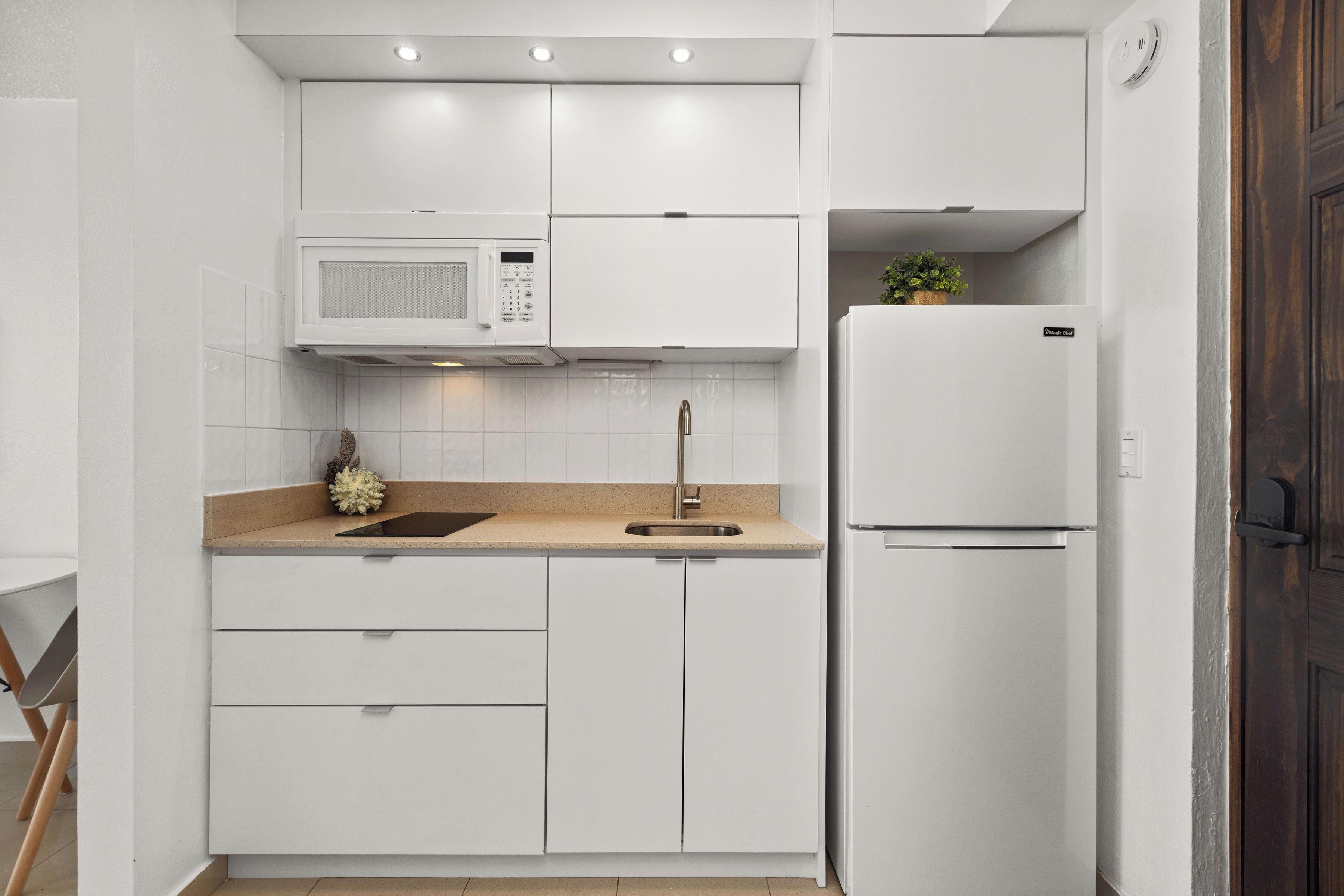 A modern kitchen with white cabinetry, a built-in microwave, a stainless steel sink, and a white refrigerator.