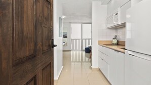 Une cuisine moderne avec des meubles blancs, une porte en bois et une vue sur un balcon doté d’une balustrade blanche.