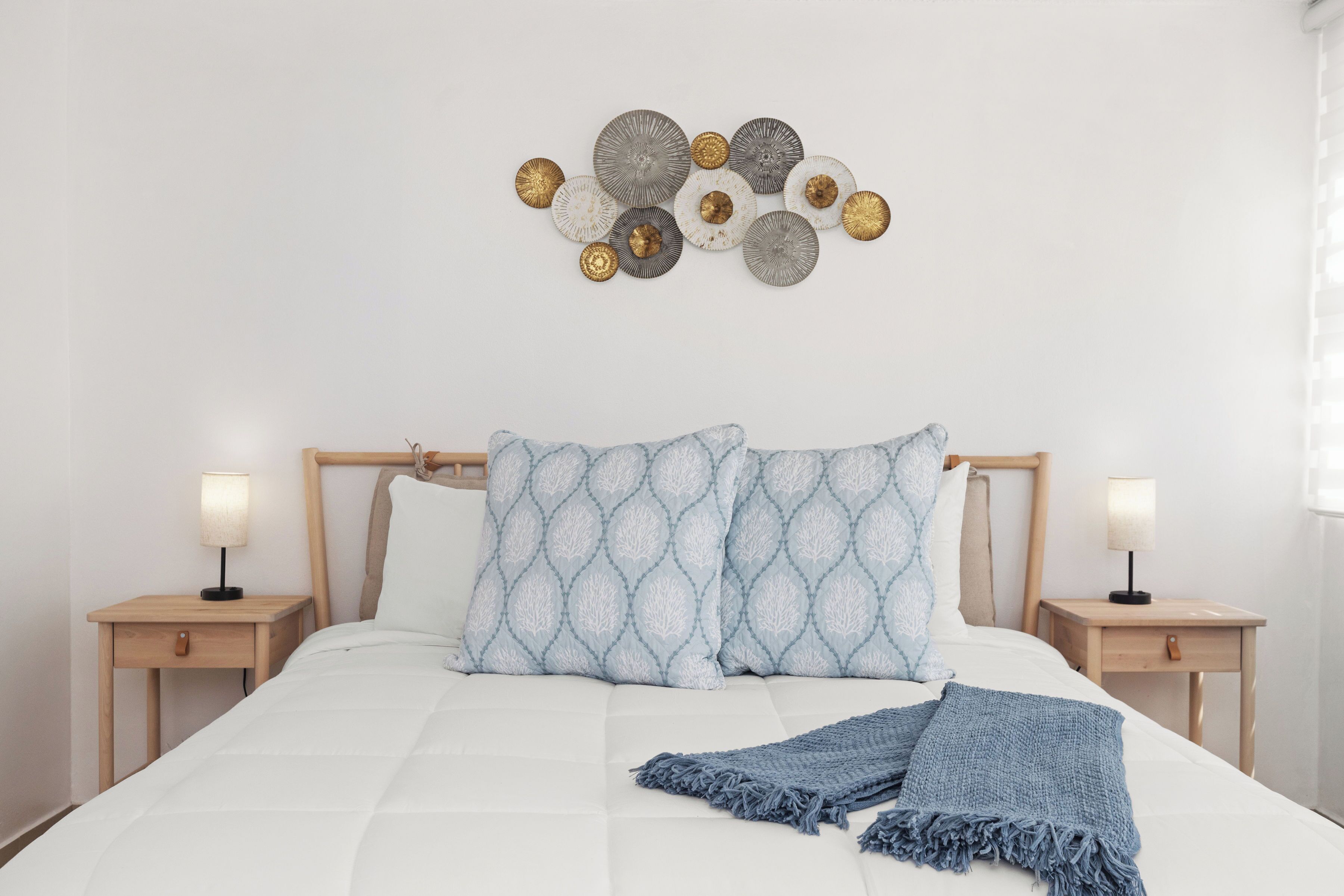 A neatly made bed with a blue blanket, two bedside tables with lamps, and a wall art piece above the bed.