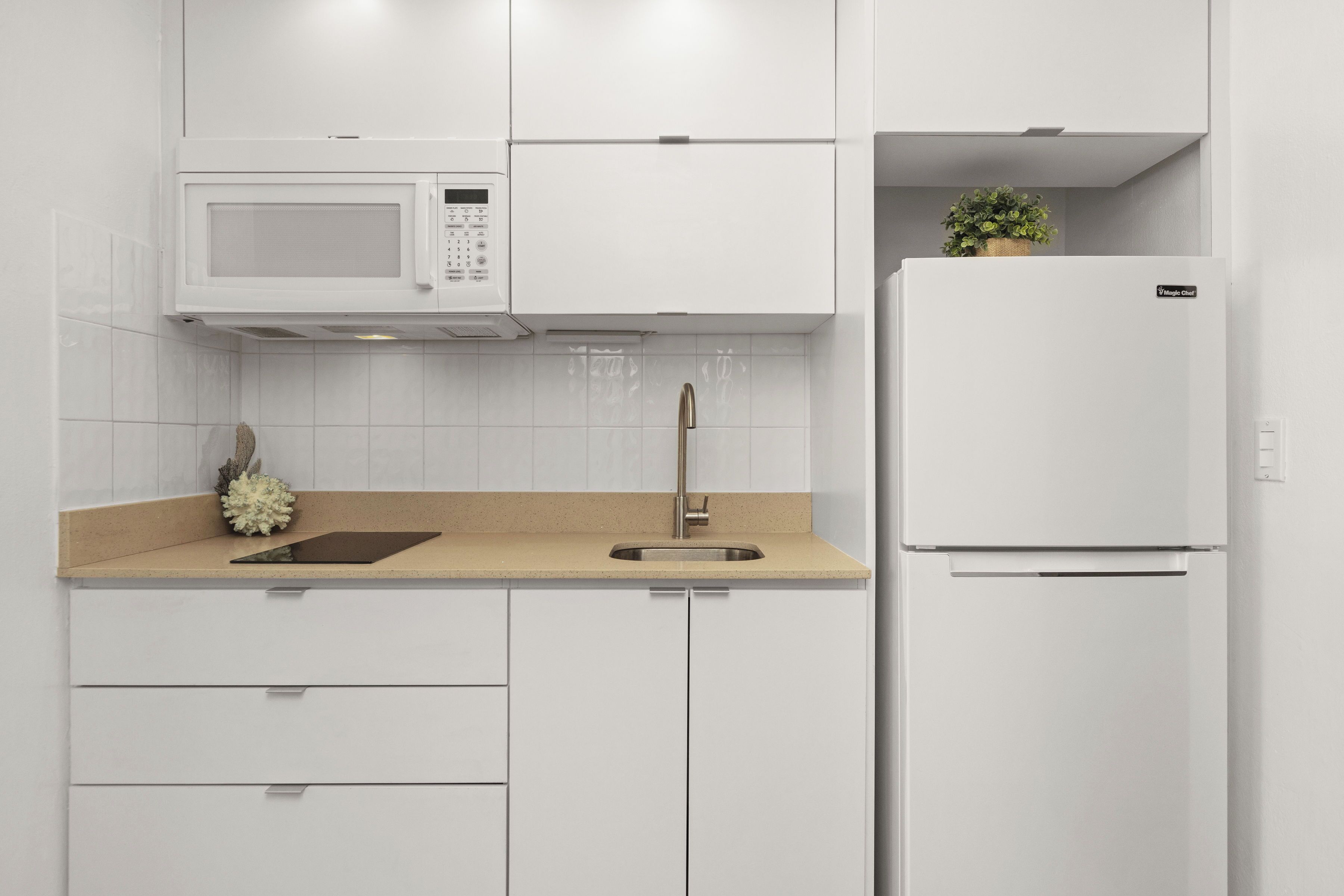 A modern kitchen with white cabinetry, a microwave, a sink, and a refrigerator.