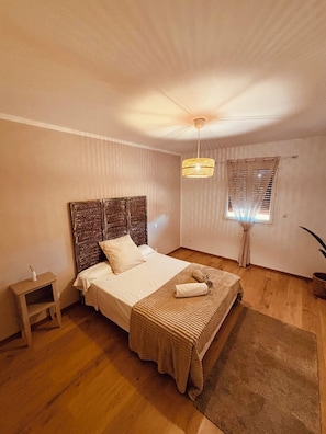 A bedroom with a bed, a nightstand, a hanging light fixture, and a window with curtains. - Charming villa in Provence, calm and relaxation for 10 people (Carpentras)