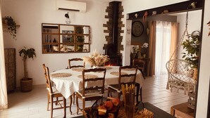 Un coin repas avec une table dressée pour quatre personnes, entourée de chaises en bois, d’un panier de fruits et d’un luminaire suspendu.