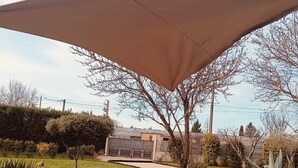 Un jardin doté d’une grande voile d’ombrage, d’un chemin de gravier et de diverses plantes.