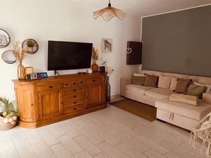 Ein Wohnzimmer mit einem Holzschrank, einem Flachbildfernseher, einer Couch und einer dekorativen Lampe.
