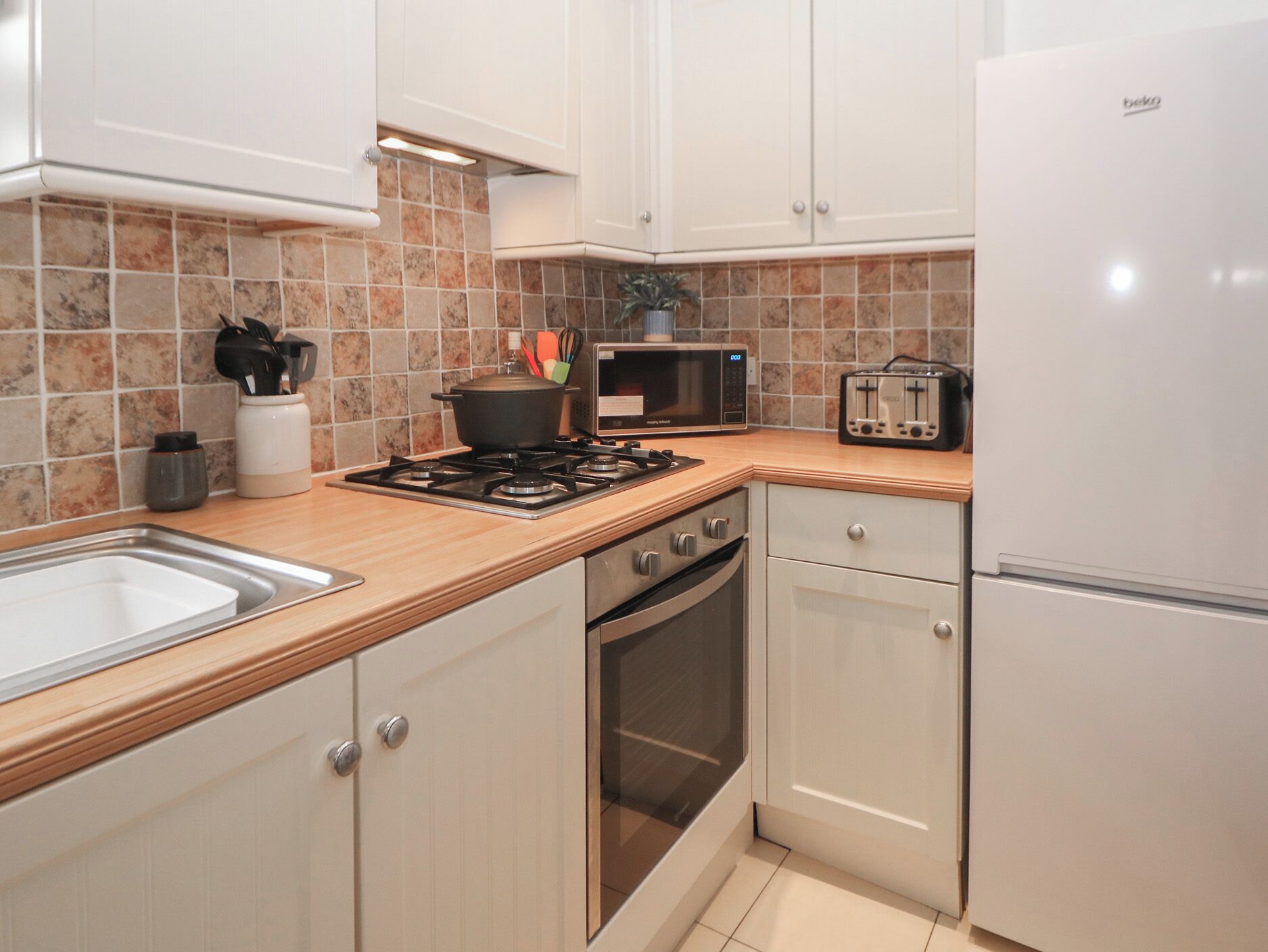 A kitchen with white cabinets, a stove, a microwave, a toaster, and a refrigerator.