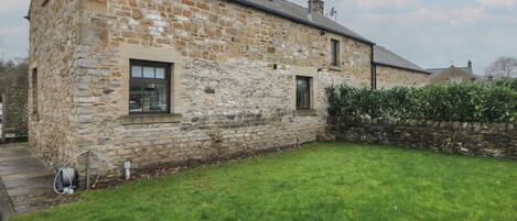 A stone building with a grassy yard and a stone wall.