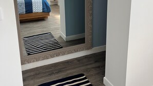 A hallway with a mirror reflecting a bedroom, a striped rug, and a white door. - Le Rameau, gite in the heart of the city, terrace, quiet street close to the Old Port. (Pornic)
