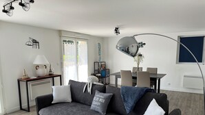 A modern living room with a grey sofa, a wooden coffee table, and a dining area with a table and chairs. - Le Rameau, gite in the heart of the city, terrace, quiet street close to the Old Port. (Pornic)