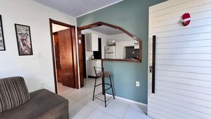 A living room with a sofa, a dining area with a table and chairs, a kitchen with cabinets and appliances, and a door with a red sign. - Casa com Piscina, Churrasqueira e Mesa de Bilhar (Caxias do Sul)