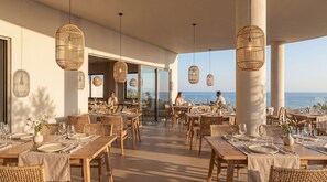 A restaurant with outdoor seating, wicker furniture, and hanging light fixtures. - VedoMare Hotel & Suites (Zakynthos)