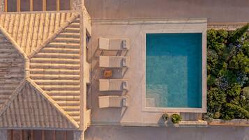 An aerial view of a hotel with a swimming pool, lounge chairs, and a tiled roof.