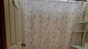 A small bathroom with a toilet, a shelf unit, and a floral-patterned shower curtain. - Casa Vacacional (Ciudad Cortes)
