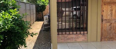 A gated entrance with a metal gate, a brick wall, and a gravel pathway leading to a building with a tiled floor.