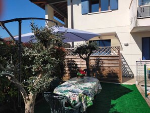Eine Terrasse im Freien mit Tisch und Stühlen, ein Holzzaun und ein Gebäude im Hintergrund.