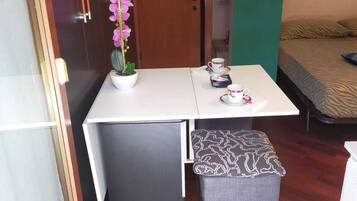 A compact room with a wooden door, a small table with a white tablecloth, a bench, and a bed with a zebra print bedspread.