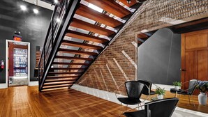 Interior moderno com escada de madeira, parede de tijolos e um espaço de estar com cadeiras e plantas.